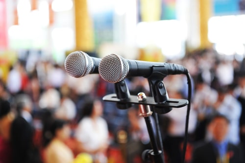 Image of microphone on stage in front of a crowed